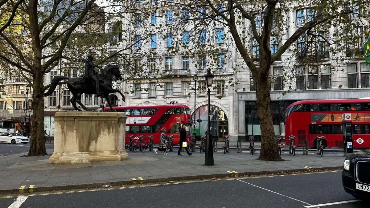 Busy executives walking though LinkedIn. Statue in fore, red bus in background.